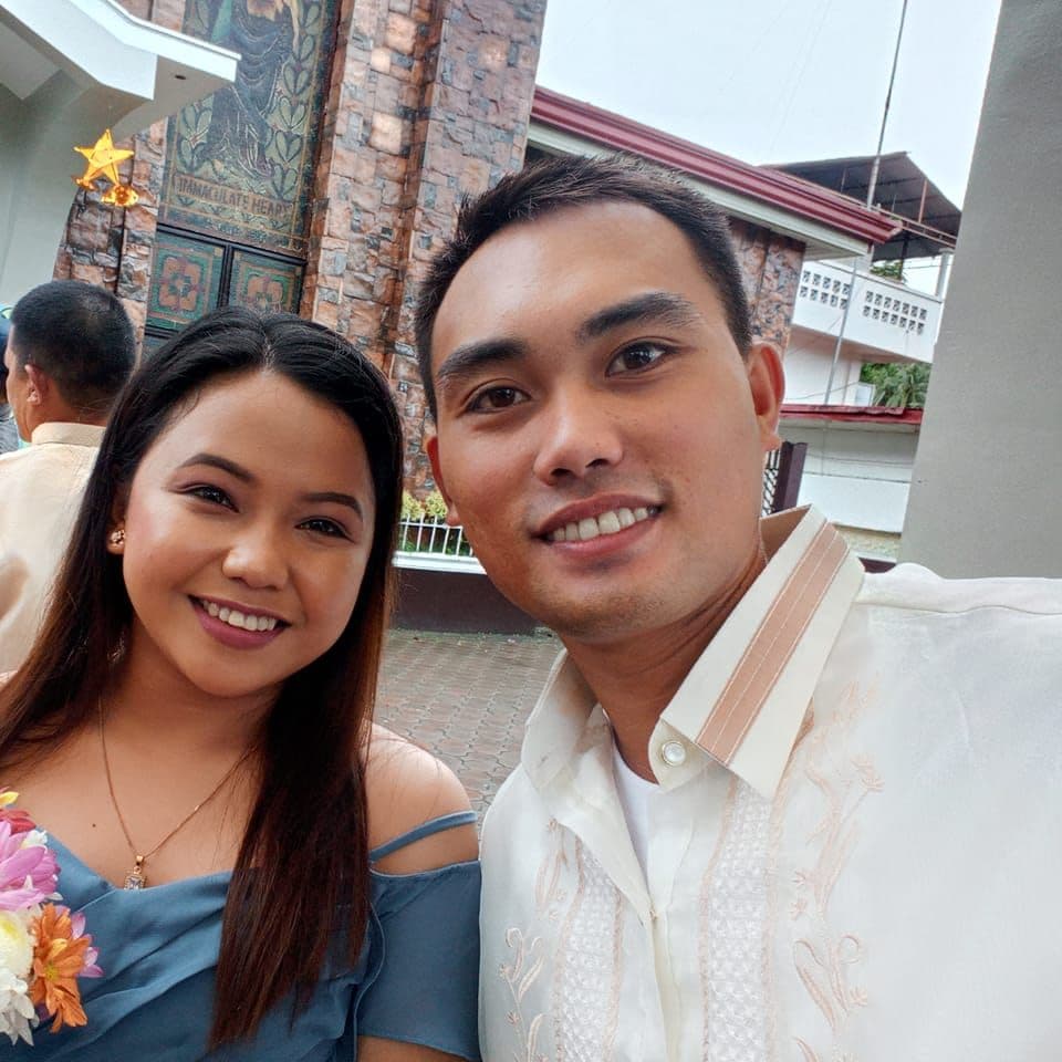 Smiling man in a Barong and woman in blue dress pose outside a church.