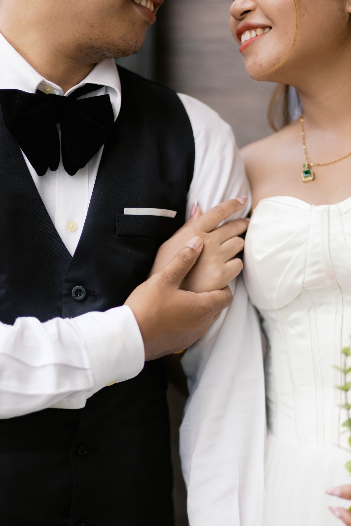 A smiling bride and groom in formal attire holding hands and looking at each other.