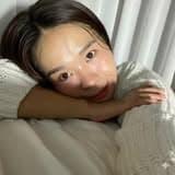 Woman with dark hair leaning her head on her arms wearing a white knit sweater.
