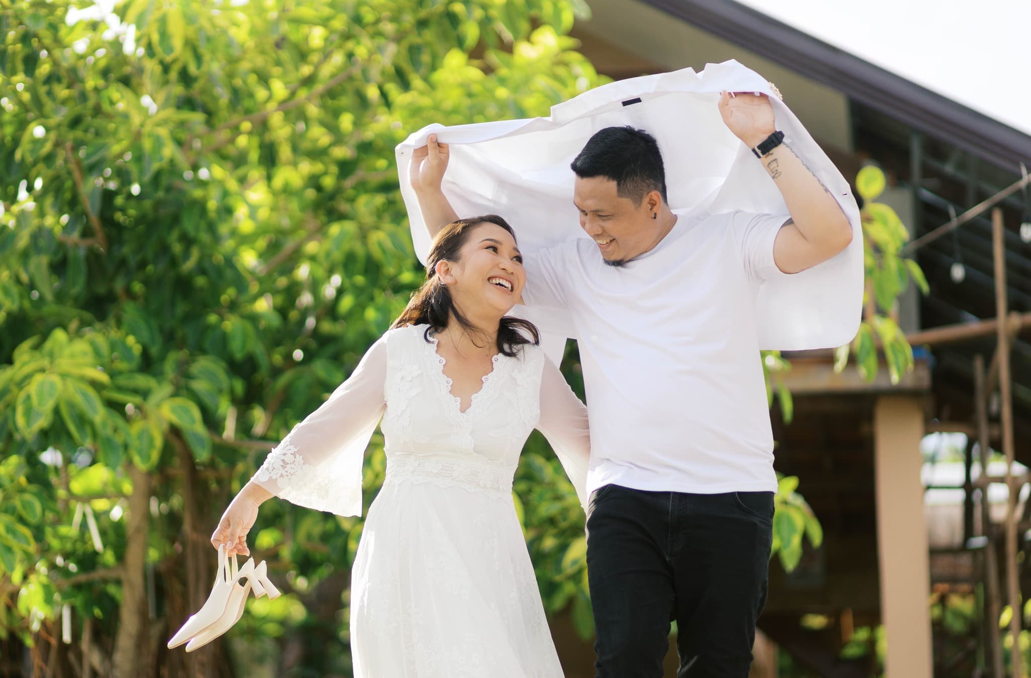 Smiling man holds a white shirt over himself and a woman holding white heels.