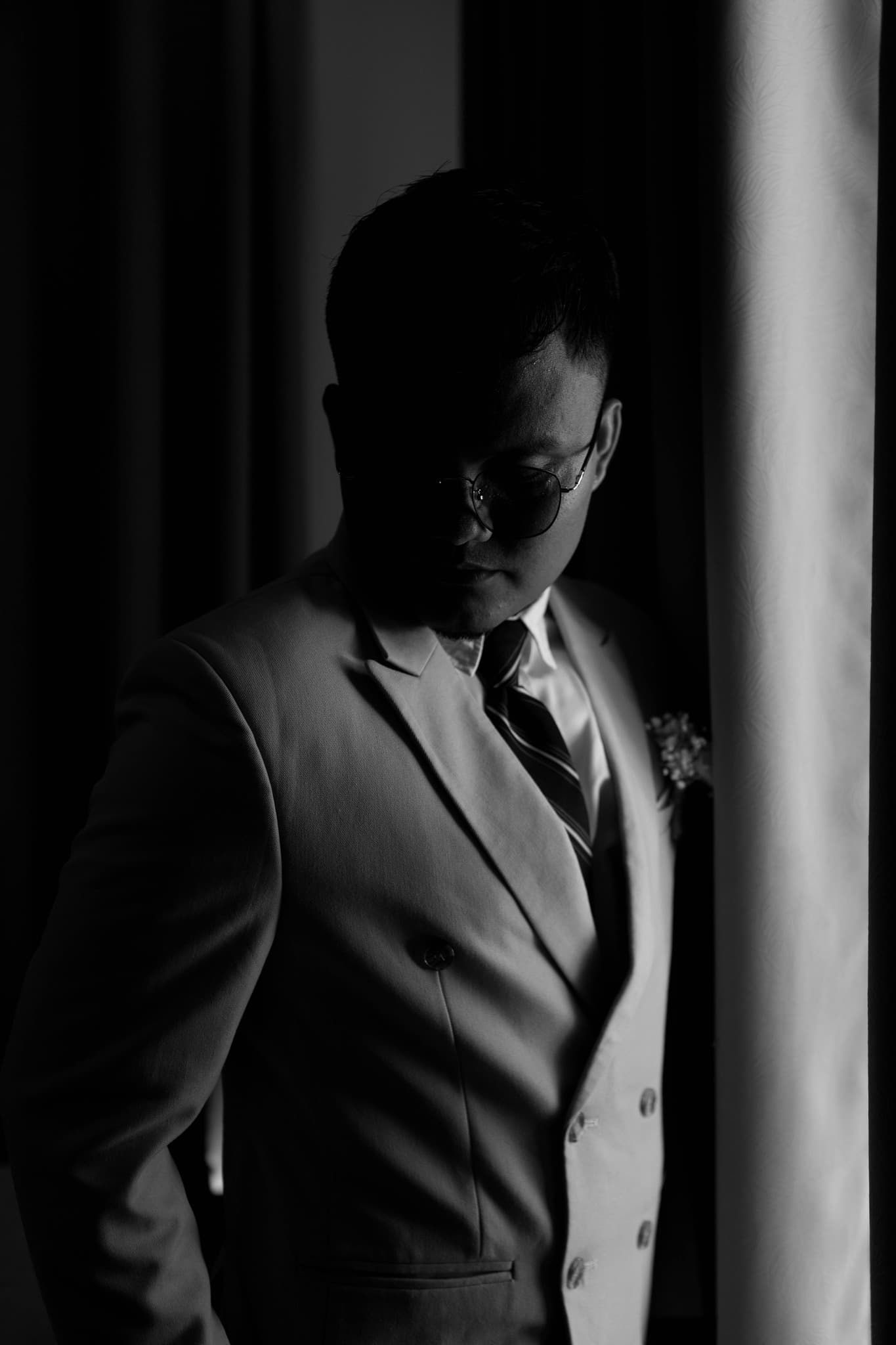 Man in a suit and glasses looking down in dramatic, low-key black and white.